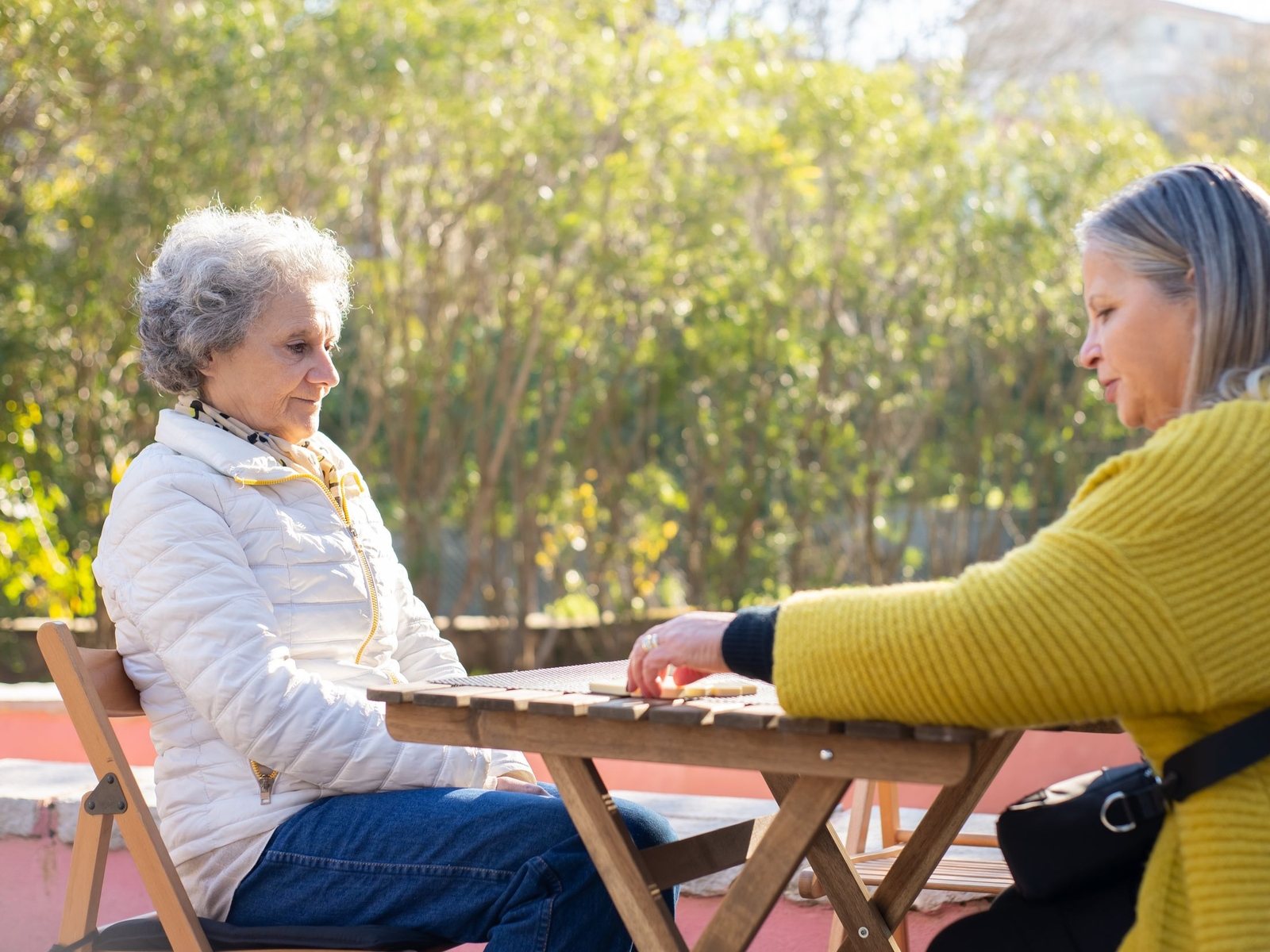 Caregiver and an older woman playing dominoes at a sunny outdoor table